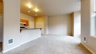 This single-floor unit offers a thoughtfully organized layout that maximizes functionality within a compact footprint. The open-concept kitchen and living area form the heart of the space, creating a seamless flow between cooking and relaxing zones. The kitchen is well-equipped with warm honey-toned wood cabinetry, dark granite-style countertops, a breakfast bar peninsula, tile flooring, and a full suite of appliances including a dishwasher, range, and refrigerator. Recessed lighting and track lighting illuminate the space effectively. The living area is generously proportioned with soft, neutral-toned carpeting underfoot and warm beige walls that lend a calm, welcoming ambiance. Large windows along the living room walls invite ample natural light and offer views of the surrounding neighborhood. A wall-mounted heating unit ensures year-round comfort. The bathroom is clean and practical, featuring tile flooring, a single-sink vanity with wood cabinetry, a full soaking tub with shower surround, and a lighted mirror. Throughout the unit, the consistent use of neutral tones and natural wood finishes creates a cohesive and inviting aesthetic, making it a comfortable and efficient living space.