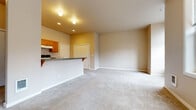 This single-floor unit offers a thoughtfully organized layout that maximizes functionality within a compact footprint. The open-concept kitchen and living area form the heart of the space, creating a seamless flow between cooking and relaxing zones. The kitchen is well-equipped with warm honey-toned wood cabinetry, dark granite-style countertops, a breakfast bar peninsula, tile flooring, and a full suite of appliances including a dishwasher, range, and refrigerator. Recessed lighting and track lighting illuminate the space effectively. The living area is generously proportioned with soft, neutral-toned carpeting underfoot and warm beige walls that lend a calm, welcoming ambiance. Large windows along the living room walls invite ample natural light and offer views of the surrounding neighborhood. A wall-mounted heating unit ensures year-round comfort. The bathroom is clean and practical, featuring tile flooring, a single-sink vanity with wood cabinetry, a full soaking tub with shower surround, and a lighted mirror. Throughout the unit, the consistent use of neutral tones and natural wood finishes creates a cohesive and inviting aesthetic, making it a comfortable and efficient living space.