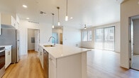 This single-story residence is designed with a clean, modern aesthetic highlighted by a bright, neutral color palette and quality finishes throughout. The open-concept kitchen serves as the centerpiece of the main living area, featuring a large center island topped with quartz countertops, an undermount sink with a pull-down faucet, and pendant lighting overhead. White shaker-style cabinetry lines the walls alongside a full suite of stainless steel appliances, including a range, microwave, dishwasher, and refrigerator. Light-toned hardwood-style flooring extends through the kitchen and flows seamlessly into the adjacent living area, which benefits from generous natural light through a large sliding glass door and windows fitted with vertical and horizontal blinds. A ceiling fan adds comfort to the living space.

The bedrooms are carpeted for warmth and comfort. The primary bedroom includes direct outdoor access and connects to a walk-in closet, while an additional bedroom also features a dedicated closet. The primary bathroom is outfitted with a dual-sink vanity topped with quartz, white shaker cabinetry, brushed nickel hardware, a large mirror, and a glass-enclosed shower. Additional rooms with hardwood-style flooring offer flexible use as a den or home office.