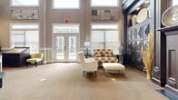 Located in Johns Creek, GA, this single-floor space offers a thoughtfully designed layout comprising a living room and kitchen, delivering a refined and welcoming atmosphere throughout.

The living room is a standout, boasting dramatically high ceilings that amplify the sense of openness. Large windows with plantation shutters invite abundant natural light, while French doors provide direct access to the outdoors. A bold, dark-mantled fireplace serves as the room's focal point, framed by elegant built-in cabinetry with geometric detailing. The two-tone walls — warm taupe above and paneled sage green below — add architectural depth, complemented by plush neutral carpeting underfoot.

The kitchen is equally impressive, featuring a herringbone-patterned hardwood floor, crisp white shaker-style cabinetry, and dark countertops. Gray subway tile backsplash lines the walls, while stainless steel appliances, including a built-in double oven, add a modern, functional edge. A bar-height counter with white seating connects the kitchen to the living area, creating a seamless flow between spaces.

Overall, the space exudes a classic yet contemporary elegance, combining rich dark wood accents, high-end finishes, and generous natural light to create a polished and inviting environment.
