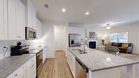 Located in Calhoun, GA, this single-story, 3-bedroom, 2-bathroom home offers a thoughtfully designed layout with warm hardwood-style flooring flowing throughout. The open-concept kitchen and living area serves as the heart of the home, anchored by a large center island with granite countertops, a dual sink, and bar seating. Crisp white shaker cabinets, subway tile backsplash, stainless steel appliances, and recessed lighting complete the kitchen's polished look. The living room features a cozy fireplace and flows seamlessly into the dining area, which is bathed in natural light from large windows. The generously sized primary bedroom includes a tray ceiling and is served by a private bathroom with a glass-enclosed walk-in shower, granite vanity, and white cabinetry. Two additional bedrooms offer natural light and ample closet space, suitable for guests or a home office. The home also includes a dedicated laundry room with full-size washer and dryer, multiple hallway closets for storage, and an attached garage. Throughout the home, neutral tones and clean lines create a bright, modern ambiance that is both functional and inviting.