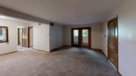 Located at 5186-5208 Everhard Rd NW in Canton, Ohio, this single-floor, 2-bedroom, 1-bathroom unit offers a practical and comfortable layout. The living area is generously sized, featuring warm neutral carpet, crisp white walls, and a standout pair of wood-framed French doors that invite natural light and provide views of the surrounding greenery. The open feel of the main living space is enhanced by a clean, uncluttered design with consistent trim work throughout.

The primary bedroom is notably spacious, offering ample room for furnishings, and is served by an impressive wall of dual bi-fold closets framed in warm wood tones, providing abundant storage. The second bedroom is equally well-proportioned, with its own wood-framed window overlooking outdoor greenery and a full bi-fold closet for storage. Both bedrooms feature soft carpeting and textured ceilings.

The bathroom is cleanly finished with tile flooring, a full tub and shower combination, a rich dark-wood vanity with drawers, a single-basin countertop sink, a large mirror, and a wall-mounted medicine cabinet. The cohesive wood accents throughout—from door frames to closet doors—give the unit a warm, unified aesthetic. The overall layout is efficient and functional, making effective use of the available floor space.
