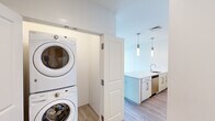 Located at 75 Braintree St in Boston's Allston neighborhood, this thoughtfully designed one-bedroom, one-bathroom residence offers a clean, contemporary aesthetic throughout. Light wood-tone flooring runs continuously across the open-plan layout, complementing the bright white walls and creating a cohesive, modern feel.

The combined kitchen and living area serves as the heart of the home. The kitchen is equipped with stainless steel appliances—including a refrigerator, range, and built-in microwave—alongside light wood cabinetry, a white quartz countertop island with an undermount sink, and sleek pendant lighting. A mosaic tile backsplash adds a refined decorative touch. A stacked washer and dryer unit is conveniently integrated near the kitchen.

The living area benefits from a sliding glass door that opens to an outdoor balcony, inviting natural light and offering views of the surrounding neighborhood. A ceiling fan provides additional comfort.

The bedroom is a well-proportioned, serene retreat featuring two large windows with outdoor views, light hardwood-style flooring, and a sliding closet with panel doors.

The bathroom is finished in a clean, minimalist style with a tub-shower combination, white tile surround, a floating vanity, and an LED-lit mirror, completing this well-appointed residence.