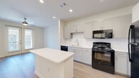 Located at 740 14th Street in Plano, TX, this one-bedroom, one-bathroom unit offers a thoughtfully designed single-floor layout that maximizes every square foot of its compact footprint. Light wood-style flooring runs throughout, creating a cohesive and modern aesthetic across all living areas.

The open-concept kitchen and living area serves as the heart of the unit. The kitchen features gray shaker-style cabinetry, white quartz countertops, a subway tile backsplash, and a full suite of black appliances including a gas range, over-the-range microwave, refrigerator, and dishwasher. A central kitchen island provides additional prep and dining space. The living area extends naturally from the kitchen and is highlighted by a ceiling fan and French doors that bring in natural light and offer access to a private balcony with exterior views.

The bedroom is a well-proportioned private retreat with a ceiling fan, a large window for natural light, and light wood-style flooring. Three closets throughout the unit provide generous storage. The bathroom features a gray vanity with a white quartz countertop, a large mirror, and a tiled tub-shower combination. A dedicated in-unit laundry area adds everyday convenience to this well-appointed Plano residence.