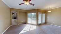 This single-floor residence offers a thoughtfully designed layout with comfortable living spaces and functional finishes throughout. The main living area is generously sized, featuring warm neutral-toned walls, plush carpeting, and crown molding that adds a refined touch. A ceiling fan provides year-round comfort, while a large sliding glass window and French door open to an outdoor deck, flooding the space with natural light and offering pleasant exterior views. A built-in shelving unit along one wall provides convenient display and storage space. Adjacent to the living area, the dining space is distinguished by a pendant light fixture, maintaining the same bright, open feel. The kitchen is outfitted with dark cabinetry, granite-style countertops, and a full suite of black appliances—including a refrigerator, range, and over-the-range microwave—all set atop rich hardwood-style flooring. The bedroom is spacious and carpeted, with ample wall space and access to a well-sized closet. The bathroom features hardwood-style flooring, dark vanity cabinetry topped with granite countertops, a large mirror with overhead lighting, and a tub-shower combination. Together, these spaces create a cohesive, comfortable living environment with practical amenities and consistent design elements throughout.