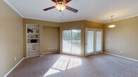 This single-floor residence offers a thoughtfully designed layout with comfortable living spaces and functional finishes throughout. The main living area is generously sized, featuring warm neutral-toned walls, plush carpeting, and crown molding that adds a refined touch. A ceiling fan provides year-round comfort, while a large sliding glass window and French door open to an outdoor deck, flooding the space with natural light and offering pleasant exterior views. A built-in shelving unit along one wall provides convenient display and storage space. Adjacent to the living area, the dining space is distinguished by a pendant light fixture, maintaining the same bright, open feel. The kitchen is outfitted with dark cabinetry, granite-style countertops, and a full suite of black appliances—including a refrigerator, range, and over-the-range microwave—all set atop rich hardwood-style flooring. The bedroom is spacious and carpeted, with ample wall space and access to a well-sized closet. The bathroom features hardwood-style flooring, dark vanity cabinetry topped with granite countertops, a large mirror with overhead lighting, and a tub-shower combination. Together, these spaces create a cohesive, comfortable living environment with practical amenities and consistent design elements throughout.
