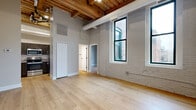 Located at 425 W Lakeside Ave in Cleveland's Lakeside neighborhood, this one-bedroom, one-bathroom unit showcases a striking combination of historic industrial architecture and contemporary upgrades. The living area features soaring ceilings with exposed wooden beam and plank construction, painted white brick walls, and light hardwood flooring throughout, creating a bright, loft-inspired atmosphere. Large black-framed windows invite abundant natural light and offer views of the surrounding urban streetscape. A ceiling fan adds both function and style to the open living space, which also features a decorative arched brick alcove as a standout architectural detail.

The kitchen is well-appointed with dark wood cabinetry, granite countertops, a subway tile backsplash, a black matte faucet, and a full suite of stainless steel appliances including a refrigerator, range, and over-the-range microwave. The bedroom is an intimate, quiet space with the same warm hardwood floors, an exposed brick column, and direct access to adjacent rooms. The bathroom features a single-vanity with wood cabinetry, a tub/shower combo, and clean white finishes. A dedicated closet completes this efficiently organized unit.