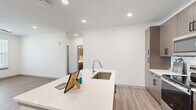 This well-designed single-floor residence offers three bedrooms and three full bathrooms, combining modern aesthetics with functional living. The open-concept kitchen and living area serves as the heart of the home, anchored by a large central island with a white quartz countertop and an undermount stainless steel sink. The kitchen is equipped with stainless steel appliances, including an electric range, over-the-range microwave, and refrigerator, all complemented by warm taupe cabinetry with sleek black hardware and a classic white subway tile backsplash. Recessed lighting throughout maintains a clean, bright atmosphere.

Light-toned wood-style flooring flows consistently across all rooms, creating a cohesive and airy feel. The bedrooms are well-proportioned, each featuring ceiling fans with integrated lighting and windows that invite natural light and outdoor views. The primary bedroom includes an en-suite bathroom outfitted with a white quartz vanity, taupe cabinetry, and mirrored medicine cabinets. A dedicated walk-in closet with multi-tiered shelving and hanging rods provides ample storage.

The additional bathrooms feature matching finishes, with tub-shower combinations and modern vanities. Crisp white walls and panel-style interior doors complete the clean, contemporary look of this thoughtfully designed residence.