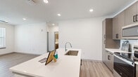 This well-designed single-floor residence offers three bedrooms and three full bathrooms, combining modern aesthetics with functional living. The open-concept kitchen and living area serves as the heart of the home, anchored by a large central island with a white quartz countertop and an undermount stainless steel sink. The kitchen is equipped with stainless steel appliances, including an electric range, over-the-range microwave, and refrigerator, all complemented by warm taupe cabinetry with sleek black hardware and a classic white subway tile backsplash. Recessed lighting throughout maintains a clean, bright atmosphere.

Light-toned wood-style flooring flows consistently across all rooms, creating a cohesive and airy feel. The bedrooms are well-proportioned, each featuring ceiling fans with integrated lighting and windows that invite natural light and outdoor views. The primary bedroom includes an en-suite bathroom outfitted with a white quartz vanity, taupe cabinetry, and mirrored medicine cabinets. A dedicated walk-in closet with multi-tiered shelving and hanging rods provides ample storage.

The additional bathrooms feature matching finishes, with tub-shower combinations and modern vanities. Crisp white walls and panel-style interior doors complete the clean, contemporary look of this thoughtfully designed residence.