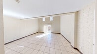 This two-floor space offers a well-organized layout spread across a generously sized main level and a more intimate upper level. The main floor immediately impresses with its dramatically high ceilings and an expansive, open living area bathed in natural light from a sliding glass door that opens to an outdoor fenced area and elevated clerestory windows above. White-painted brick accent walls add texture and character throughout, complementing the clean, neutral color palette. Light ceramic tile flooring runs consistently throughout, lending a cohesive, easy-to-maintain finish. The galley-style kitchen is efficiently designed with dark cabinetry, granite-look countertops, a double stainless steel sink, a range, and a full-size refrigerator — providing ample functionality within a compact footprint. Three bathrooms across both floors offer convenience, with at least one featuring a granite-topped vanity and an adjoining closet, and another with a full tub-shower combination. A wooden staircase with a dark-stained balustrade leads to the upper level, where a ceiling fan, tiled hallway, and additional rooms provide comfortable secondary living space. The upper floor's open landing overlooks the lower level, enhancing the sense of vertical space throughout. The overall ambiance is bright, clean, and functional.