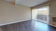 Located at 1919 E Birch St in Brea, California, this one-bedroom, two-bathroom residence offers a well-planned single-level layout designed to maximize functionality. The living room serves as the heart of the home, featuring wood-style laminate flooring, a textured ceiling, a ceiling fan, and a sliding glass door with vertical blinds that opens to a private balcony, allowing natural light to fill the space. The galley-style kitchen is thoughtfully appointed with white cabinetry, dark granite countertops, black appliances including a refrigerator, electric range, and dishwasher, and wood-style flooring that ties the space together seamlessly. An adjacent dining area provides a natural flow between the kitchen and living spaces. The bedroom is carpeted for comfort, features a window with exterior views, and is connected to a hallway with a dedicated closet. The two bathrooms are finished with dark granite vanity tops and wood-style flooring; one includes a shower-tub combination. Neutral warm-toned walls throughout create a cohesive and inviting ambiance. A connecting hallway with panel-style doors links the private areas of the home with ease.