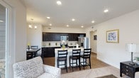 This single-floor residence showcases an open-concept design that seamlessly connects the kitchen, dining, and living areas into one cohesive and functional space. The kitchen is a standout feature, outfitted with rich, dark espresso cabinetry that extends to the ceiling, providing generous storage. Light countertops offer a striking contrast against the dark cabinets, while stainless steel appliances—including a refrigerator, range, and built-in microwave—add a modern, polished touch. A peninsula with seating for three serves as a natural divider between the kitchen and the adjoining living spaces, making it ideal for casual dining or entertaining. Recessed lighting throughout the ceiling ensures consistent, bright illumination across the open floor plan. The dining area accommodates a full table and chairs, anchored by an elegant chandelier overhead. Durable wood-look flooring runs throughout the main areas, transitioning to a soft area rug in the living space, where a patterned accent chair adds a touch of personality. The neutral color palette and clean lines create a modern yet inviting ambiance throughout.