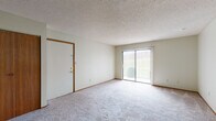 This single-floor unit offers a practical and straightforward layout designed for comfortable everyday living. The living area is bright and open, featuring neutral carpet, white walls, and a sliding glass door fitted with vertical blinds that allows natural light to flow in and provides views of the surrounding greenery outside. A second carpeted space, accessible via an interior door, offers versatility and includes a large sliding-door closet with warm wood-toned panels, making it well-suited as a bedroom or additional living area.

The kitchen is equipped with rich, dark wood cabinetry both above and below the countertops, offering ample storage. A stainless steel double sink, electric coil range, and a ventilation hood are among the functional features, while hardwood-style flooring adds a warm contrast to the lighter cabinetry tones. A pass-through opening connects the kitchen to adjacent areas.

A carpeted bedroom with a window provides natural light and a quiet retreat. The full bathroom includes a wood-toned vanity with a light countertop, a standard toilet, and a tub and shower combination unit, complemented by hardwood-style flooring. Throughout the unit, textured ceilings and neutral tones create a cohesive, understated ambiance.