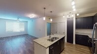 This thoughtfully designed single-floor residence offers a cohesive and contemporary aesthetic throughout. The open-concept kitchen serves as the heart of the home, anchored by a central island with a double stainless steel sink and granite countertops. Dark espresso cabinetry provides generous storage and contrasts elegantly with the light stone surfaces. Stainless steel appliances, including a refrigerator, range, and microwave, complete the modern kitchen suite. Pendant lighting and a track lighting system illuminate the space with warm, layered light.

The living area flows seamlessly from the kitchen, featuring warm hardwood-style flooring, a ceiling fan, and a window that brings in natural light. The open layout creates a spacious, airy feel that connects the main living zones effortlessly.

Two bathrooms are finished to a consistent standard, each featuring granite-topped dark vanities, large mirrors, and bright vanity lighting. One bathroom includes a tub-shower combination, while the other offers an expansive vanity layout with direct access to a bedroom.

A generously sized walk-in closet with multiple shelving rods and natural light from a window provides ample organization space. Hardwood-style flooring runs through the main areas, with plush carpet in the closet and bedroom zones, offering a comfortable and practical contrast throughout the residence.