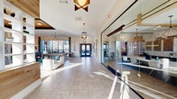 Located at 1035 Strensall Lane in Charlotte, NC, this amenity center at Sonderly at the Reservoir offers a thoughtfully designed, single-floor community space that blends modern aesthetics with practical functionality. The welcoming entrance features large-format tile flooring, soaring ceilings, decorative pendant lighting, warm wood-paneled accent walls, and built-in shelving — setting an inviting tone from the moment you arrive. A glass-walled conference or leasing office sits just off the entry corridor, bathed in natural light.

The expansive living lounge is the heart of the space, showcasing coffered ceilings with rich wood inlays, floor-to-ceiling windows that flood the room with natural light and exterior views, a fireplace, and an eclectic mix of contemporary seating. A billiards table, bar-height dining, and a beverage station make this an ideal gathering space for residents.

The two fitness rooms are well-appointed and distinct in purpose. One room features cardio equipment including treadmills and ellipticals alongside a textured tile accent wall and large windows. The second room is dedicated to strength and functional training, housing cable machines, kettlebells, medicine balls, battle ropes, and cycling and rowing equipment. A glass-panel garage door opens the space to the outdoors, enhancing ventilation and ambiance throughout the fitness area.