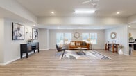 Located at 6539 Pegram Farm Rd in Lewisville, NC, this thoughtfully designed single-floor space offers a cohesive and functional layout finished with light-toned luxury vinyl plank flooring throughout. The expansive living room is a welcoming centerpiece, featuring vaulted ceilings, recessed lighting, a ceiling fan, and multiple windows fitted with white blinds that allow abundant natural light. The open floor plan creates a generous sense of space, complemented by neutral walls and clean architectural lines. The combined dining room and kitchen area provides a practical and inviting setting. The kitchen is equipped with rich dark wood cabinetry, granite countertops, a tile backsplash, and black appliances, while the adjacent dining area accommodates multiple seating arrangements, making it well-suited for group gatherings. A dedicated coffee station and built-in counter space add functional versatility to this zone. The private office features a wrap-around granite-topped desk, recessed lighting, and a window providing natural light — ideal for focused work. A secondary entry door with a window panel connects the space to the outdoors. Throughout, the design balances a warm, modern aesthetic with practical amenities, creating an inviting and highly functional environment.