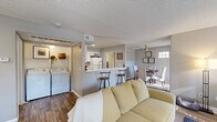 This single-floor residence offers a thoughtfully designed layout that balances comfort and functionality throughout. The open-concept living area is anchored by wood-look flooring, neutral gray walls, and a textured ceiling, creating a warm and inviting atmosphere. Natural light filters in through multiple windows, including an arched accent window, enhancing the bright and airy feel of the space.

The kitchen is a standout feature, equipped with white cabinetry, white appliances, and a striking quartz countertop that extends into a peninsula-style breakfast bar with seating for two. This seamlessly connects the kitchen to the living and dining areas, making it ideal for entertaining.

The dining area accommodates a full-sized table and benefits from a ceiling fan, a window, and access to a sliding glass door dressed with sheer curtains, allowing for ample natural light.

Two bedrooms provide comfortable retreats; the primary bedroom features plush carpeting and a closet, while the second bedroom includes a large sliding-door closet with built-in shelving. The full bathroom offers a marble-look quartz vanity countertop and a well-lit mirror.

A dedicated in-unit laundry area houses a full-sized washer and dryer, adding everyday convenience to this well-rounded residence.
