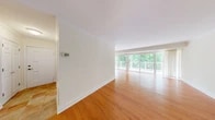 This well-appointed 2-bedroom, 2-bathroom single-floor home offers a thoughtfully designed layout with a welcoming open-plan living and dining area at its heart. Rich hardwood flooring flows throughout the main living spaces, complemented by clean white walls, crown molding, and an abundance of natural light. The living and dining area is a standout, featuring expansive floor-to-ceiling sliding glass doors that open directly onto a private outdoor deck, where lush, mature tree canopy creates a tranquil, nature-immersed backdrop.

The kitchen is equipped with warm oak cabinetry, light countertops, tile flooring, and a full suite of white appliances including a gas range, over-the-range microwave, and refrigerator, providing a practical and efficient cooking space.

The generously sized primary bedroom features parquet-style hardwood flooring, a large window framing serene greenery, and a spacious walk-in closet with dual wire shelving for ample storage. The second bedroom also benefits from hardwood flooring and natural light. Both bedrooms are served by well-appointed bathrooms, one featuring a tub-shower combination with elegant marble-style tile surround. The home's serene wooded setting and open connection to the outdoors create a calm, nature-connected ambiance throughout.