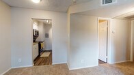 This single-story unit offers a practical and well-organized layout designed for comfortable everyday living. The kitchen is efficiently arranged with white cabinetry, light stone-finish countertops, a stainless steel refrigerator, dishwasher, and a gas range with an overhead microwave. Wood-look flooring runs throughout the kitchen and connecting areas, providing a clean, durable surface. An electrical panel is conveniently integrated into the kitchen space, and track lighting ensures the area is well-lit.

The living area transitions from wood-look flooring to plush wall-to-wall carpeting, creating a comfortable, cozy atmosphere. A hallway connects the main living space to the rest of the unit, with carpeted flooring continuing into the bedrooms. Each bedroom features ceiling fans with light fixtures, neutral-toned walls, and windows fitted with horizontal blinds that allow natural light to filter in while maintaining privacy. Views from the windows overlook surrounding greenery.

The bathroom includes wood-look flooring, a bright, open feel with access to adjacent spaces, and a textured wall finish consistent with the rest of the unit. Throughout, textured ceilings add a consistent design element, and neutral wall tones create a clean, understated ambiance suited to a variety of furnishing styles.