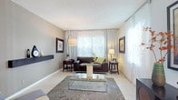 This single-floor residence offers a thoughtfully designed layout that balances comfort and functionality across its key living spaces. The living room serves as the heart of the home, featuring light-toned tile flooring, neutral gray walls, and large windows dressed with sheer patterned curtains that allow generous natural light to fill the room. A floating dark wood shelf adds a modern architectural accent, while the glass-top coffee table and dark leather seating contribute to a contemporary aesthetic.

The galley-style kitchen is efficient and clean, outfitted with white cabinetry, granite-look countertops, tile flooring, and white appliances including a full-size refrigerator and dishwasher, providing ample workspace and storage.

Adjacent to the entry, the dining area features a chandelier overhead and sheer-curtained windows on two sides, creating a bright and welcoming atmosphere for meals.

The primary bedroom features wood-look flooring and a spacious layout with room for a full dresser suite. The secondary bedroom also includes wood-look flooring, wall-mounted shelving, and a dedicated desk area. A full bathroom with a tub-shower combination completes the floor plan.