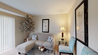 This single-floor residence at 25400 Rockside Rd in Bedford, Ohio offers a well-organized and functional layout across several distinct living areas. The living room serves as the central gathering space, featuring plush wall-to-wall carpeting, warm neutral-toned walls, and a large sliding glass door fitted with vertical blinds that allows generous natural light and outdoor views. The kitchen is efficiently designed with oak cabinetry, light countertops, tile flooring, a stainless steel sink, and white appliances including a gas range and dishwasher, providing ample storage and workspace. Adjacent to the kitchen, the dining area accommodates a four-seat table beneath a classic chandelier, creating a welcoming spot for meals. The bedroom is a comfortable retreat with soft carpeting, a textured ceiling, and access to a dedicated walk-in closet, offering practical storage solutions. The bathroom features tile flooring, oak cabinetry with overhead storage, a vanity with a wide countertop, and a full mirror. A separate home office provides a quiet, carpeted workspace complete with built-in desk capacity and wall art. Throughout the residence, the consistent use of neutral tones, carpet, and warm lighting creates a cohesive and inviting atmosphere.