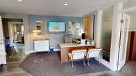 Located in Kent, WA, this leasing office and amenity facility offers a thoughtfully designed, single-floor layout that combines professional functionality with resident-focused conveniences. The reception area serves as the welcoming centerpiece, featuring a sleek front desk with wall-mounted display screens, vibrant abstract artwork, and modern orange-accented guest seating. Frosted glass partitions elegantly separate the reception from adjacent office spaces, maintaining an open yet professional atmosphere. A secondary room serves as a comfortable lounge and private office, complete with wood-look flooring, a white futon sofa, a compact work desk, a wall-mounted mini-split system, and colorful framed artwork that adds warmth to the neutral tones. The fitness center is generously sized and well-appointed, housing a row of treadmills, stationary bikes, a recumbent bike, a full dumbbell rack, stability balls, resistance equipment, and yoga mats. Large windows flood the exercise space with natural light, while ceiling fans maintain airflow throughout. A bold typographic accent wall reinforces the fitness theme, and dark rubberized flooring provides a durable, functional surface. Together, these spaces deliver a polished, amenity-rich environment tailored to both leasing operations and resident wellness.
