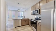 Located at 199 Dickenson St in Columbus, Ohio, this efficiently designed unit offers a well-appointed single-floor layout that maximizes every square foot. The open-concept kitchen and living area serves as the heart of the space, featuring warm-toned cabinetry, granite countertops, a full suite of stainless steel appliances — including a dishwasher, range, and over-the-range microwave — and a subway tile backsplash. A peninsula with pendant globe lighting anchors the kitchen, providing both prep space and a natural gathering point. Light wood-look flooring runs throughout, lending a clean, cohesive aesthetic. The living area receives natural light through large windows dressed with blinds. A bedroom offers additional natural light through a generously sized window, accompanied by a spacious walk-in closet with wire shelving for organized storage. Two bathrooms complete the layout, one featuring a full tub/shower combination with dark oil-rubbed bronze fixtures set against crisp white surroundings. Neutral gray wall tones and white trim provide a modern, move-in-ready finish throughout the entire unit.