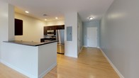 Located at 46 River St in Boston's Mattapan neighborhood, this single-floor unit offers a thoughtfully designed open-concept layout with a clean, contemporary aesthetic. The living area is spacious and bright, featuring light-toned hardwood flooring and soft blue-gray walls that create a calm, neutral atmosphere. Large windows frame lush tree views, filling the space with natural light and a sense of connection to the outdoors.

The kitchen is positioned at the heart of the unit, defined by a peninsula with a dark countertop that separates it from the living area. Dark espresso cabinetry is paired with a full suite of stainless steel appliances, including a gas range, over-the-range microwave, dishwasher, and refrigerator, providing a polished, functional cooking space.

The bedrooms are generously proportioned, each finished with soft carpeting and neutral tones. Large windows in the bedrooms continue the theme of natural light and outdoor views of surrounding trees, creating peaceful, restful retreats.

The bathroom features tile flooring in a neutral stone tone, a full tub-shower combination with white subway tile surround, and clean, minimal fixtures. A hallway with recessed lighting connects the rooms, and an accessible electrical panel is conveniently located near the entry.