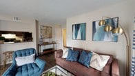 This single-floor residence offers a thoughtfully designed layout with cohesive finishes and a warm, modern aesthetic carried throughout each room. The living room serves as the heart of the home, featuring a tiled fireplace with a clean white mantel, bold blue-and-white patterned drapery, and rich hardwood-style flooring that extends throughout the space. Framed abstract artwork in teal tones adds a stylish touch, complementing the neutral warm-beige walls.

The dining area connects seamlessly to the living space and is anchored by a round wooden table surrounded by upholstered chairs, with a ceiling fan overhead and large sliding door access that brings in natural light. The kitchen is galley-style and well-equipped, featuring dark espresso cabinetry, subway tile backsplash, light countertops, and black appliances including a range and refrigerator.

Both bedrooms are generously proportioned, each with hardwood-style flooring, ceiling fans with integrated lighting, and ample closet access. The primary bedroom features a tufted upholstered headboard and walk-in closet entry. The two bathrooms mirror each other in finish, offering dark vanity cabinetry, wide mirrors with bar lighting, and neutral countertops. One bathroom includes a shower-tub combination. The overall ambiance is clean, cohesive, and move-in ready.