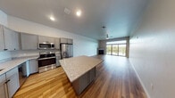 This well-designed one-bedroom, one-bathroom unit in Kimberly, WI offers a thoughtful single-floor layout that balances modern finishes with functional living. The open-concept kitchen and living area serves as the heart of the home, featuring warm hardwood-style flooring that flows throughout. The kitchen is outfitted with grey shaker-style cabinetry, granite countertops, a central island, and a full suite of stainless steel appliances including a French door refrigerator, electric range, built-in microwave, and dishwasher. The expansive living area is anchored by a fireplace and a ceiling fan, with floor-to-ceiling sliding glass doors that open to a balcony and frame sweeping waterfront views, flooding the space with natural light. The bedroom is generously sized with a ceiling fan, a large window overlooking the water, and access to a spacious walk-in closet with wire shelving. The bathroom features granite countertops, a grey vanity, and hardwood-style flooring consistent with the rest of the unit. A dedicated in-unit laundry room with side-by-side washer and dryer and additional wire shelving adds everyday convenience to this modern, move-in-ready home.