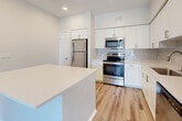 This single-floor, 2-bedroom, 2-bathroom residence offers a clean, modern aesthetic throughout, unified by light-toned wood-style flooring and crisp white walls. The open-concept kitchen is a standout feature, equipped with stainless steel appliances—including a refrigerator, range, and microwave—complemented by white shaker cabinetry, a subway tile backsplash, and a white quartz peninsula that provides additional counter space and separates the kitchen from the living area. The living room is bright and airy, featuring a ceiling fan, a built-in accent niche, and sliding glass doors that open to a private balcony with views of palm trees. Both bedrooms are comfortably sized with wood-style flooring, large windows that invite natural light, and ceiling fans. The primary bedroom includes a walk-in closet outfitted with wire shelving systems for organized storage. The two bathrooms maintain the home's modern palette, with white vanities, large mirrors, and a shower-tub combination. A dedicated laundry room houses a full-size top-loading washer and dryer. Three hallways and two closets round out the thoughtfully designed layout, ensuring practical flow and ample storage throughout.