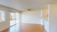 This single-floor unit offers a clean, functional layout with consistent wood-style flooring running throughout the living areas and bedrooms, creating a cohesive and easy-to-maintain interior. The open living and dining area is generously sized, featuring a ceiling fan with integrated light fixture and a textured ceiling. A sliding glass door floods the space with natural light and provides direct access to an outdoor balcony, while a secondary window further enhances the bright, airy atmosphere.

The kitchen is designed in a galley configuration, outfitted with white cabinetry extending to the ceiling for ample storage. Appliances include a gas cooktop, wall oven, and over-the-range microwave. A pass-through counter connects the kitchen to the living area, supporting an open feel.

The bedrooms each feature wood-style flooring, ceiling fans, and natural light from windows fitted with blinds or vertical slat coverings. One bedroom includes a sliding closet with a full-width door panel. The bathroom presents a clean, all-white finish with a shower-tub combination, a window above the tub for ventilation, a wall-mounted mirror, and a single-basin vanity.