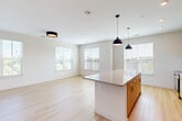 This well-appointed 2-bedroom, 2-bathroom residence in Peabody, MA offers a thoughtfully designed single-floor layout with a clean, modern aesthetic. The open-concept living and kitchen area serves as the heart of the home, featuring light wood-tone flooring, crisp white walls, and large windows dressed with horizontal blinds that invite generous natural light and outdoor views. The kitchen is outfitted with warm wood cabinetry, granite countertops, stainless steel appliances including a range, microwave, and refrigerator, a white subway tile backsplash, and a central island with pendant lighting overhead. The spacious living area flows seamlessly from the kitchen, enhanced by additional windows on multiple walls. The primary bedroom offers comfortable carpeting, a ceiling fan, a dedicated window, and direct access to a private en-suite bathroom with wood-tone vanity cabinetry and a walk-in closet. The second bedroom is bright and well-proportioned with its own window and light flooring. Both bathrooms are finished with light, neutral tones; one features a full tub-shower combination with white tile surround and built-in shelving. The unit also includes a dedicated laundry space, five closets for ample storage, and two hallways connecting the rooms efficiently.