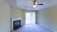 This single-floor residence offers a well-organized layout with a variety of functional spaces thoughtfully arranged throughout. The living room serves as the centerpiece of the home, highlighted by a classic white-mantled fireplace with a sleek black surround, plush carpeting, and a tray ceiling that adds architectural interest and a sense of height. A ceiling fan centered within the tray ceiling provides both style and comfort. Sliding glass doors flood the room with natural light and open to an outdoor space, offering a pleasant connection to the exterior.

The kitchen is positioned toward the back of the floor plan and is equipped with standard appliances, cabinetry, and countertop workspace. Adjacent areas provide additional functional zones, including spaces that appear suited for dining or multipurpose use. The floor plan, as seen in the dollhouse view, reveals a logical flow between rooms with clear separation of living and utility areas. Neutral warm tones carry throughout the walls and flooring, lending the home a cohesive and inviting ambiance. Overall, this single-level residence combines practical layout design with comfortable living features.