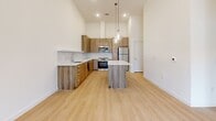Located at 8350 W US Highway 290 in Austin, TX, this one-bedroom, one-bathroom unit offers a well-designed layout with contemporary finishes throughout. The open-concept kitchen is a standout feature, showcasing warm wood cabinetry, a textured tile backsplash, white quartz countertops, and a full suite of stainless steel appliances including a range, microwave, dishwasher, and refrigerator. A central kitchen island with pendant lighting provides additional prep space and a focal point for the living area. Soaring ceilings amplify the sense of space throughout the unit, and light-toned hardwood-style flooring flows seamlessly through every room. The bedroom is a bright, serene retreat, featuring tall ceilings and a window that brings in natural light and views of the surrounding neighborhood. A dedicated closet provides organized storage adjacent to the bedroom. The bathroom is finished with large-format stone-look tile flooring, a glass-enclosed walk-in shower with tiled surround, and a wood-accented vanity with a white countertop. Clean white walls and consistent design choices throughout give the space a cohesive, modern aesthetic suited for comfortable everyday living in Southwest Austin.