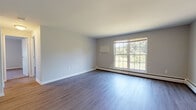 Located in Amherst, MA, this single-floor residence offers a clean, functional layout designed for comfortable living. The spacious living area is highlighted by durable hardwood-style flooring, neutral gray walls, and large multi-pane windows that flood the room with natural light and frame views of the surrounding trees and greenery. Baseboard heating runs along the perimeter, ensuring warmth throughout the cooler New England seasons.

The galley-style kitchen is efficiently designed with white cabinetry providing ample storage, light countertops, a stainless steel refrigerator, a range with oven, and a dishwasher — offering a complete set of appliances for everyday use.

The bedrooms are carpeted for comfort and each features a sliding-door closet with built-in shelving. Windows in the bedrooms bring in natural light while baseboard heaters maintain a consistent temperature. The bathroom is bright and clean, appointed with a tub-shower combination, a white vanity with storage, and light wood-style flooring.

A utility area near the entry houses the electrical panel, and the open layout connects the living, kitchen, and bedroom spaces in a practical flow. This residence offers a straightforward, move-in-ready environment in the heart of Amherst.