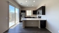 Located at 150 E Warner Rd in Gilbert, AZ, this 530-square-foot, single-story unit offers a well-designed 1-bedroom, 1-bathroom layout with modern finishes throughout. Dark hardwood-style flooring runs consistently across all rooms, creating a cohesive and contemporary aesthetic. The kitchen is a standout feature, equipped with a full suite of stainless steel appliances including a refrigerator with ice maker, electric range, over-the-range microwave, and dishwasher. Rich, dark espresso cabinetry contrasts sharply with light quartz countertops, and a peninsula provides additional prep and dining space. Recessed lighting and a large sliding glass door allow abundant natural light into the kitchen and living area. The 140-square-foot bedroom features a ceiling fan, a high horizontal window, and an additional side window, providing natural light and ventilation. A secondary room offers a window with a street view and multiple electrical outlets, providing versatility as a home office or storage space. The bathroom includes a combined tub and shower with a glass sliding door, a dark vanity with a light countertop, and a tall privacy window. The unit's neutral wall tones and clean architectural lines contribute to a bright, functional, and move-in-ready living environment.