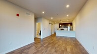This thoughtfully designed single-floor unit offers a seamless open-concept layout that connects the living area directly to the kitchen, creating a spacious and cohesive environment. Rich hardwood-style flooring flows throughout the main living spaces, complemented by crisp white walls and recessed lighting that keep the interior bright and inviting.

The kitchen is a standout feature, showcasing dark espresso cabinetry, white quartz countertops, and a full suite of stainless steel appliances including a refrigerator, range, microwave, and dishwasher. A large peninsula with an undermount sink and stylish pendant lighting adds both functionality and visual appeal. A subway tile backsplash provides a clean, modern finish.

A distinctive sliding barn door adds a contemporary architectural touch, leading to additional spaces within the unit. The bedroom is carpeted for comfort and features a generous window fitted with blinds, allowing natural light and outdoor views. A dedicated hallway connects the living areas to the bathroom, which includes a full tub and shower combination, a dark-cabinetry vanity with a white countertop, and neutral tile flooring. A private balcony door in the living area further enhances the sense of openness and connection to the outdoors.
