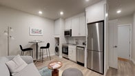 This efficiently designed single-floor residence maximizes every square foot with a smart, open-concept layout and modern finishes throughout. Light wood-style flooring flows seamlessly across the living, kitchen, and dining areas, creating a cohesive and airy feel.

The kitchen is a standout feature, outfitted with sleek white cabinetry extending to the ceiling for ample storage, a subway tile backsplash, and a full suite of stainless steel appliances including a refrigerator, dishwasher, range with oven, and built-in microwave. An in-unit washer is conveniently integrated into the kitchen area. A compact dining counter with bar seating provides a casual space for meals.

The living area offers an open, flexible layout with recessed lighting overhead. A dedicated workspace nook features a built-in wall-mounted desk positioned beneath a window, bringing in natural light — ideal for working from home.

The bedroom is a cozy, well-appointed retreat with overhead cabinetry for additional storage and a window that allows in natural light. The full bathroom features clean white tile surrounding a bathtub and shower combo, grey floor tile, and brushed nickel fixtures, maintaining the home's modern and neutral aesthetic throughout.