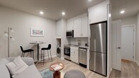 This efficiently designed single-floor residence maximizes every square foot with a smart, open-concept layout and modern finishes throughout. Light wood-style flooring flows seamlessly across the living, kitchen, and dining areas, creating a cohesive and airy feel.

The kitchen is a standout feature, outfitted with sleek white cabinetry extending to the ceiling for ample storage, a subway tile backsplash, and a full suite of stainless steel appliances including a refrigerator, dishwasher, range with oven, and built-in microwave. An in-unit washer is conveniently integrated into the kitchen area. A compact dining counter with bar seating provides a casual space for meals.

The living area offers an open, flexible layout with recessed lighting overhead. A dedicated workspace nook features a built-in wall-mounted desk positioned beneath a window, bringing in natural light — ideal for working from home.

The bedroom is a cozy, well-appointed retreat with overhead cabinetry for additional storage and a window that allows in natural light. The full bathroom features clean white tile surrounding a bathtub and shower combo, grey floor tile, and brushed nickel fixtures, maintaining the home's modern and neutral aesthetic throughout.