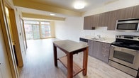 Located at 4040 26th Ave SW in Seattle's South Seattle neighborhood, Unit 504 is a thoughtfully designed residential unit that blends modern finishes with functional living spaces. The open-concept kitchen and living area serves as the heart of the unit, featuring light wood-look flooring that extends throughout. The kitchen is equipped with stainless steel appliances — including a range, microwave, and refrigerator — complemented by rich wood-toned cabinetry, light countertops, and a stainless steel sink. A freestanding kitchen island with a dark countertop provides additional prep and dining space. Natural light fills the living area through a generous window that frames views of the surrounding neighborhood. The bedroom is a calm, carpeted retreat with a wide window, a baseboard heater, and ample closet storage. Hallway storage and additional closet space offer practical organization throughout the unit. A full bathroom features a shower-tub combination, while a dedicated in-unit laundry closet houses a stacked washer and dryer for added convenience. The unit's clean, neutral palette and modern design elements create a comfortable and contemporary living environment.