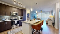 This thoughtfully designed 2-bedroom, 2-bathroom residence offers a cohesive open-concept floor plan that maximizes both functionality and comfort. The kitchen serves as the heart of the home, showcasing rich dark-walnut cabinetry, a herringbone tile backsplash, stainless steel appliances, and a large granite-topped island with bar seating — all illuminated by stylish pendant lighting and a track lighting system. The kitchen flows seamlessly into the living room, which features warm hardwood-style flooring, a ceiling fan, and expansive floor-to-ceiling windows that bathe the space in natural light. The primary bedroom is generously sized, complete with plush carpeting, a ceiling fan, and its own dedicated walk-in closet fitted with built-in shelving and a hanging rod. The en-suite primary bathroom features dark cabinetry, dual granite vanities, large-format tile flooring, and a glass-enclosed walk-in shower. The second bedroom is equally comfortable with carpet, a ceiling fan, and ample natural light. A second full bathroom mirrors the same refined finishes. Two dedicated closets provide excellent storage throughout. The overall ambiance is modern yet warm, with consistent upscale finishes unifying every room.