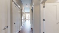 This 490 square foot apartment offers a thoughtful blend of style and functionality. The heart of the home is a striking kitchen, featuring sleek white cabinetry that extends to the ceiling, maximizing storage space. Stainless steel appliances, including a refrigerator, oven, and microwave, add a modern touch. A distinctive mosaic tile backsplash in shades of grey adds visual interest and complements the overall color scheme.

The living area seamlessly connects to the kitchen, creating an open-concept feel. Rich, warm-toned wood flooring extends throughout the space, adding warmth and continuity. Recessed lighting in the ceiling provides ample illumination, while natural light filters in through nearby windows.

A sliding barn-style door leads to the spacious 440 square foot bedroom, offering a unique architectural element and space-saving solution. The bathroom, while not visible in the image, completes the efficient floor plan of this compact yet well-designed apartment. The neutral color palette and clean lines contribute to a contemporary aesthetic, making this space feel larger than its actual square footage suggests.