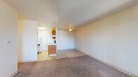 This single-floor unit offers a practical and straightforward layout centered around an open-concept living and kitchen area. The living space is finished with neutral-toned carpet and features a ceiling fan with light fixture overhead, complemented by a textured popcorn ceiling. A sliding glass door provides access to an outdoor balcony area and allows natural light to fill the room, while a wall-mounted air conditioning unit and baseboard heaters ensure year-round climate control.

The kitchen adjoins the living area in an open-plan arrangement, featuring warm-toned wood cabinetry, white coil-burner electric range, a refrigerator, and an overhead ventilation hood. Light tile flooring distinguishes the kitchen from the carpeted living spaces. A peninsula-style counter provides a natural visual boundary between the two areas.

The bedroom is a well-proportioned, carpeted room with a large window overlooking outdoor greenery, a built-in closet with rod and shelf, and baseboard heating. Natural light enters generously through the window.

The bathroom includes a full tub and shower surround accented with retro yellow tile, a wood-trimmed vanity, toilet, and tile flooring, completing the unit's classic aesthetic.