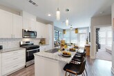 This thoughtfully designed single-floor residence offers a seamless blend of modern aesthetics and functional living. The open-concept kitchen is a standout feature, showcasing crisp white shaker cabinetry, granite countertops, a classic subway tile backsplash, and a full suite of stainless steel appliances including a gas range, microwave, refrigerator, and dishwasher. A generously sized island with seating provides both additional prep space and a casual dining area, illuminated by sleek pendant lighting overhead.

The kitchen flows naturally into the living area, which is bright and welcoming thanks to large windows dressed with white blinds and warm golden drapes that invite abundant natural light. A ceiling fan adds comfort, while wood-style flooring runs throughout the main living spaces, creating a cohesive and contemporary feel.

The bedroom is a comfortable retreat, featuring plush carpeting, a ceiling fan, and well-proportioned windows that continue the home's bright and airy character. It connects directly to a private bathroom, complete with a glass-enclosed walk-in shower finished with subway tile, granite vanity countertops, and convenient access to a dedicated walk-in closet with built-in shelving and hanging space. Every detail of this residence reflects a clean, modern design sensibility.