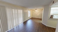 This single-floor unit is finished with dark hardwood-style flooring that runs consistently throughout the living areas, bedrooms, and hallways, providing a cohesive and polished look. The textured ceilings add subtle character to each room, while clean white baseboards offer a crisp contrast against the warm, neutral-toned walls.

The open living area is generously proportioned, featuring a ceiling fan with light fixture and a large sliding glass door dressed with vertical blinds that allow for adjustable natural light. An additional window further brightens the space. The layout flows naturally toward the entryway, which includes a front door and access to adjacent rooms.

The kitchen is equipped with white cabinetry, light speckled countertops, a double stainless steel sink, and a distinctive skylight-style ceiling panel that floods the workspace with bright, diffused light.

The bedrooms are well-sized, each with neutral walls, dark flooring, and vertical blinds or windows for natural light. At least one bedroom includes a sliding closet, providing practical storage.

The bathroom features a full tub-shower combination with chrome fixtures and a vanity area with a speckled countertop, undermount sink, and wall-mounted mirror cabinet, completing this functional and neatly presented space.