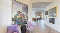 Located at 4404 W Cedar Brooke Ln in Rogers, Arkansas, this well-appointed single-floor community space offers a thoughtfully designed interior that balances contemporary aesthetics with welcoming warmth. The open layout is anchored by soaring vaulted ceilings that amplify the sense of spaciousness throughout the main gathering area.

A dramatic floor-to-ceiling stacked stone fireplace serves as the central focal point of the lounge, complemented by large-format slate-toned tile flooring and a curated seating arrangement featuring leather and upholstered furnishings. Floor-to-ceiling black-framed glass doors and windows flood the interior with natural light while providing direct access to an outdoor patio area.

A built-in wet bar with light wood cabinetry and a white quartz countertop with barstool seating adds a functional entertaining element. Adjacent to the main lounge, a gallery-style corridor showcases an eclectic collection of large-scale artwork and framed pieces displayed against clean white walls with warm wood-look tile flooring.

The space also includes a glass-partitioned room visible from the main area, likely a fitness or multipurpose room. The overall ambiance is modern yet inviting, blending natural stone textures, contemporary furnishings, and vibrant art to create a refined communal environment.