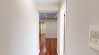 This efficient single-floor, 1-bedroom, 1-bathroom unit is thoughtfully laid out to maximize every square foot of its compact footprint. Rich, warm-toned hardwood floors run throughout the hallways and living areas, lending a sense of continuity and warmth to the space. Recessed lighting installed in the ceilings provides consistent, even illumination across the hallways and main rooms, complemented by clean white trim and neutral wall tones that keep the interior feeling bright and open.

The galley-style kitchen is a functional highlight, featuring light wood cabinetry, granite-style countertops, a stainless steel sink, and white gas appliances. White square wall tiles with a bold black checkerboard accent border add a classic, retro character to the kitchen. Light ceramic floor tiles offer a practical contrast to the hardwood found elsewhere in the unit.

The bedroom is a cozy, well-proportioned room with the same warm hardwood flooring and soft neutral walls, offering a calm and restful environment. A closet with a sliding door provides essential storage.

The bathroom is finished with full white square wall tiles, a combination bathtub and shower, a white vanity with chrome fixtures, and a mirrored medicine cabinet, delivering a clean and functional space. Two hallways connect the rooms, contributing to an efficient and logical floor plan throughout the unit.