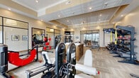 Located at 780 Doss Dr in Marysville, Ohio, this fitness center offers a thoughtfully designed, single-floor layout that accommodates a full range of workout options. The main exercise area is generously sized, featuring elevated ceilings with crown molding, recessed lighting, and a tray ceiling detail that adds architectural refinement to the space. Neutral-toned walls and patterned carpet tiles throughout create a clean, professional atmosphere.

The primary workout room is extensively equipped with cardio machines including treadmills, ellipticals, stair climbers, and stationary bikes, as well as a robust selection of strength training equipment such as cable machines, selectorized stations, and a sled. A dedicated free weights section features kettlebells, medicine balls, resistance bands, and TRX suspension trainers organized on wall-mounted racks. Multiple wall-mounted TVs are positioned throughout for entertainment during workouts.

Large windows with wood-slat blinds allow ample natural light to fill the space, while glass-panel partition walls provide visual openness between zones. A secondary room offers an open, carpeted area ideal for stretching or group fitness. Additional amenities include restroom access and a centrally located resource station. The facility presents a polished, fully functional environment suited for a wide variety of fitness goals.