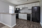 Located at 110 Penner St in Winston-Salem, NC, this single-story residence offers a straightforward, functional layout designed for comfortable living. The interior is finished in a consistent soft gray palette throughout, creating a calm and cohesive atmosphere across all rooms.

The living area features plush carpeting, crown molding, a ceiling fan with a light fixture, and direct access to an exterior door, allowing natural light to filter in through multiple slatted blinds. A baseboard heating system provides supplemental warmth. The open connection between the living space and kitchen makes the area feel practical and well-integrated.

The kitchen has been updated with white cabinetry fitted with brushed nickel hardware, granite-look laminate countertops, a double stainless steel sink, and wood-look vinyl plank flooring. Black appliances, including a refrigerator, range, microwave, and dishwasher, provide a sharp contrast to the bright cabinetry.

The bedrooms continue the carpeted flooring and neutral wall tones, with crown molding and ceiling-mounted light fixtures. One bedroom includes a wall-mounted air conditioning unit and a window with natural light access.

The bathroom features a full tub and shower combo with clean white surroundings and brushed nickel fixtures, maintaining the home's consistent, tidy aesthetic throughout.